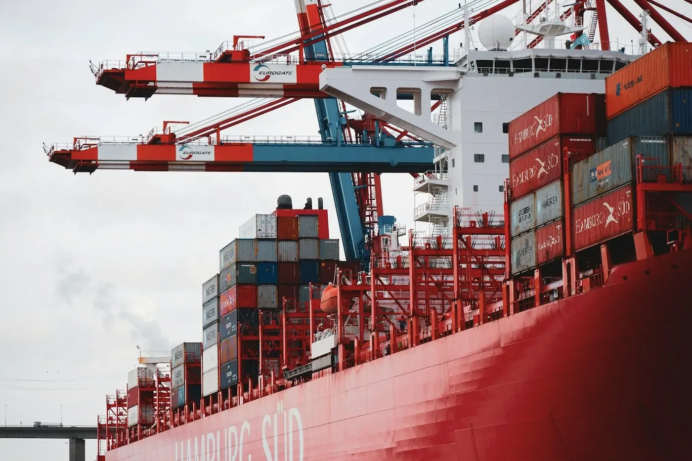 Containerschiff im Hafen, darüber die Ausleger zweier Verladekräne