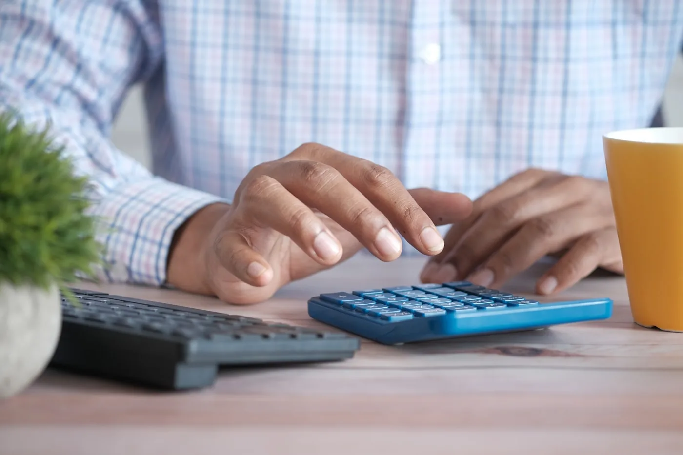 Person am Schreibtisch tippt auf einem blauen Taschenrechner neben einer Tastatur
