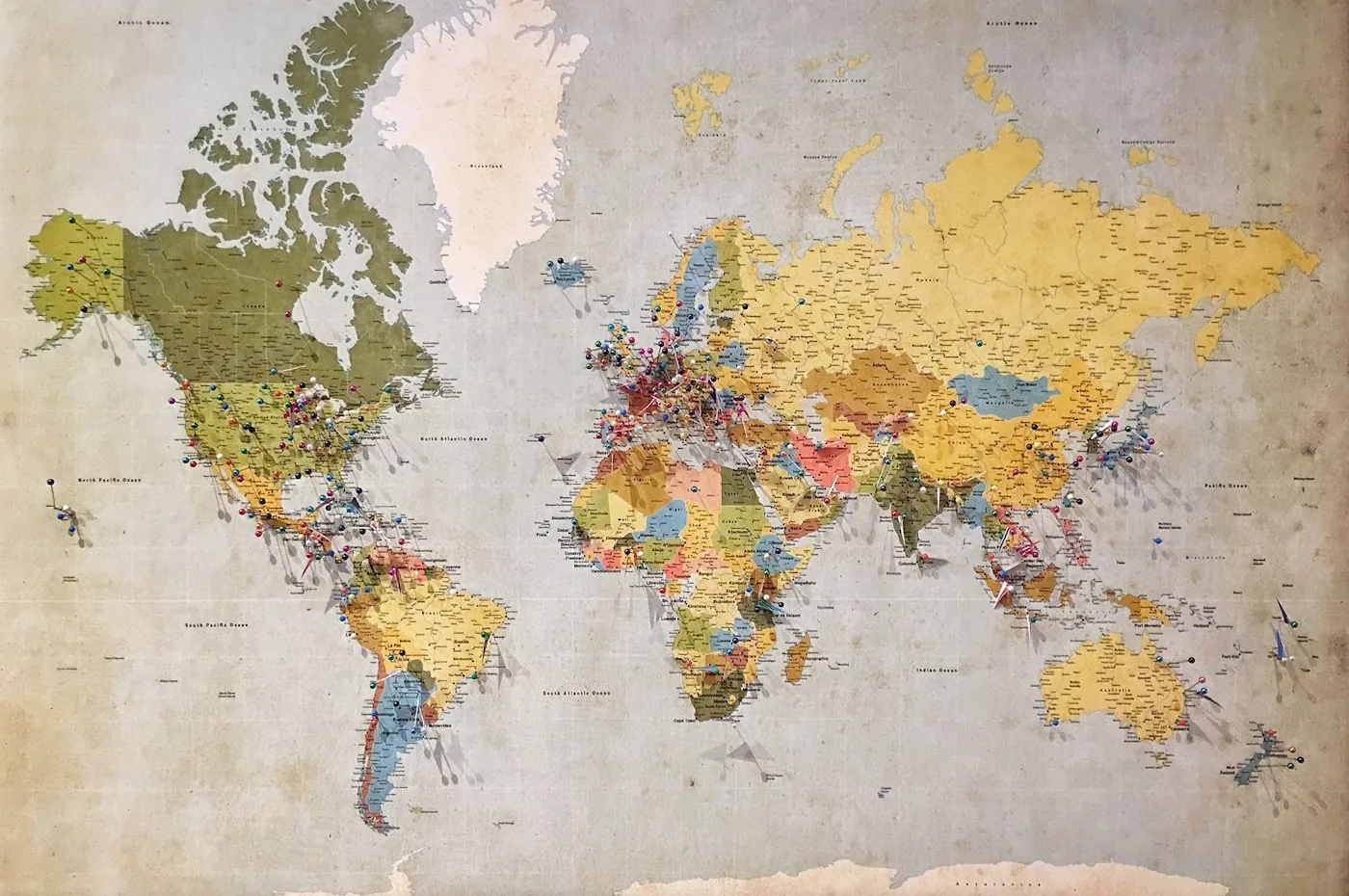 Vergilbte Weltkarte an einer Wand, übersät mit bunten Stecknadeln