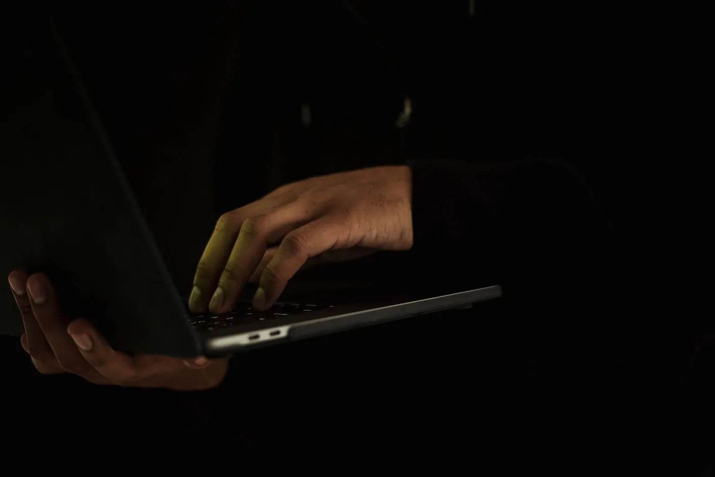 Hände an einem aufgeklappten Laptop im Dunkeln