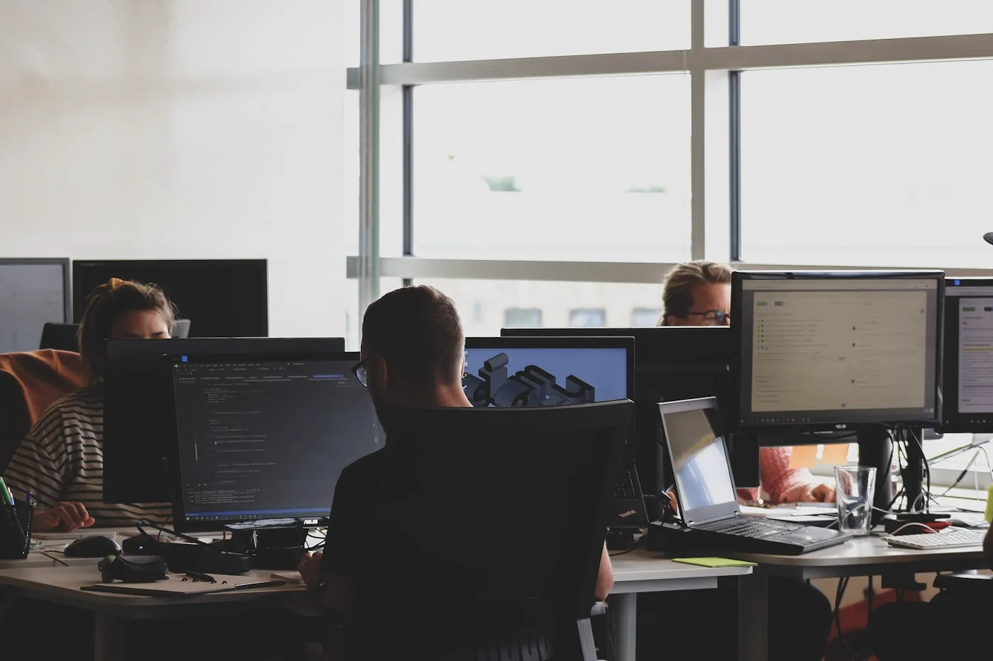 Several people working at monitors with open code in a bright open-plan office