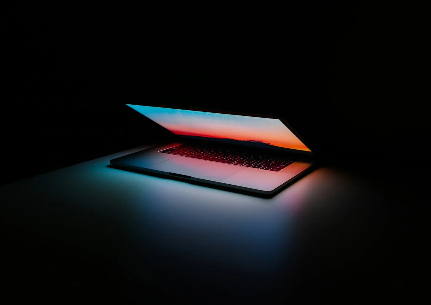 A half-open laptop in a dark room, its screen glowing orange and blue