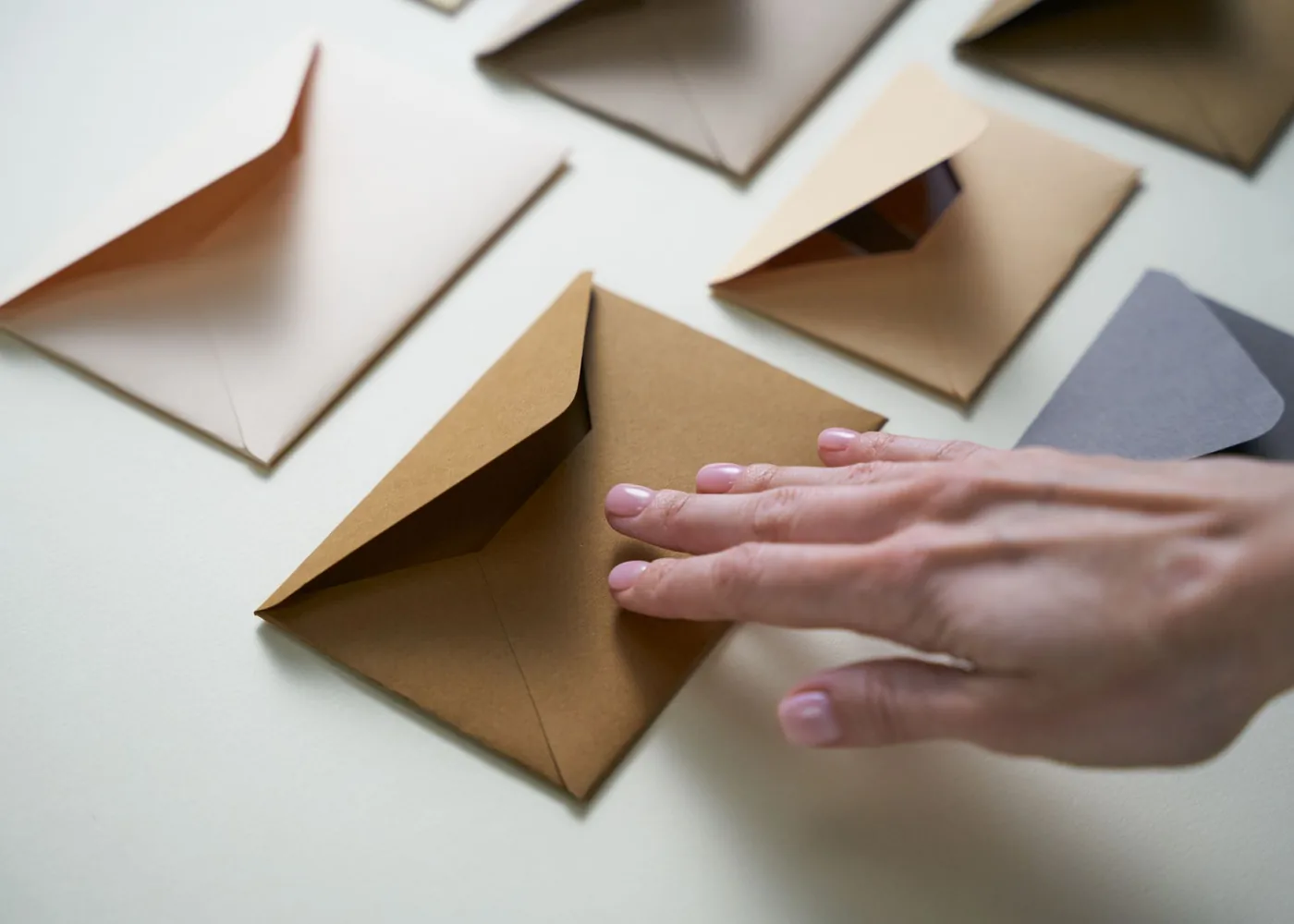 A hand sorting brown and light envelopes on a table