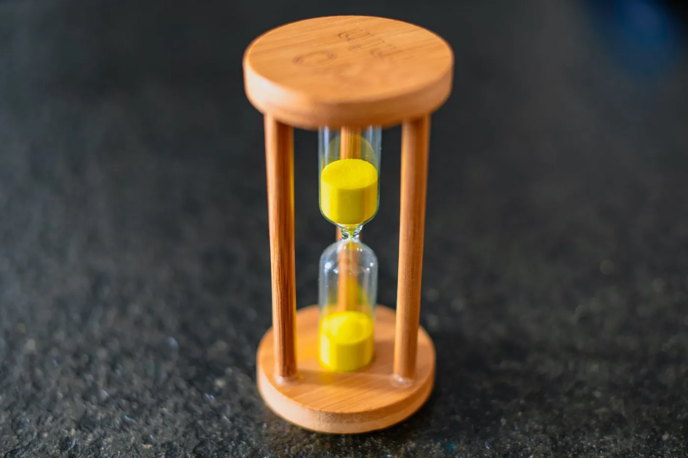 A wooden hourglass with yellow sand on a dark table
