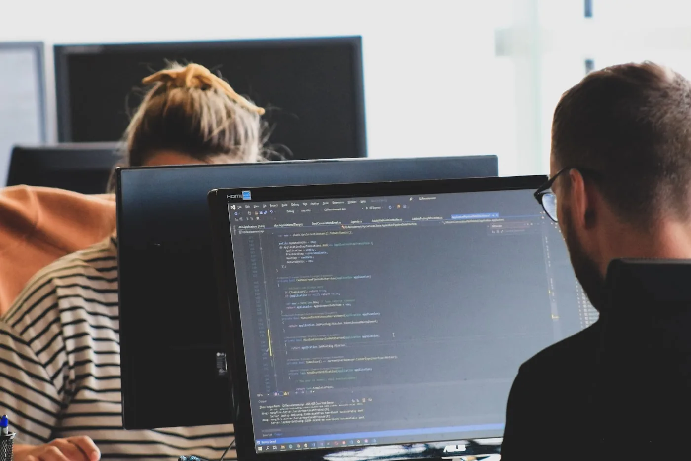 Zwei Personen arbeiten im Büro an Bildschirmen mit geöffnetem Code-Editor