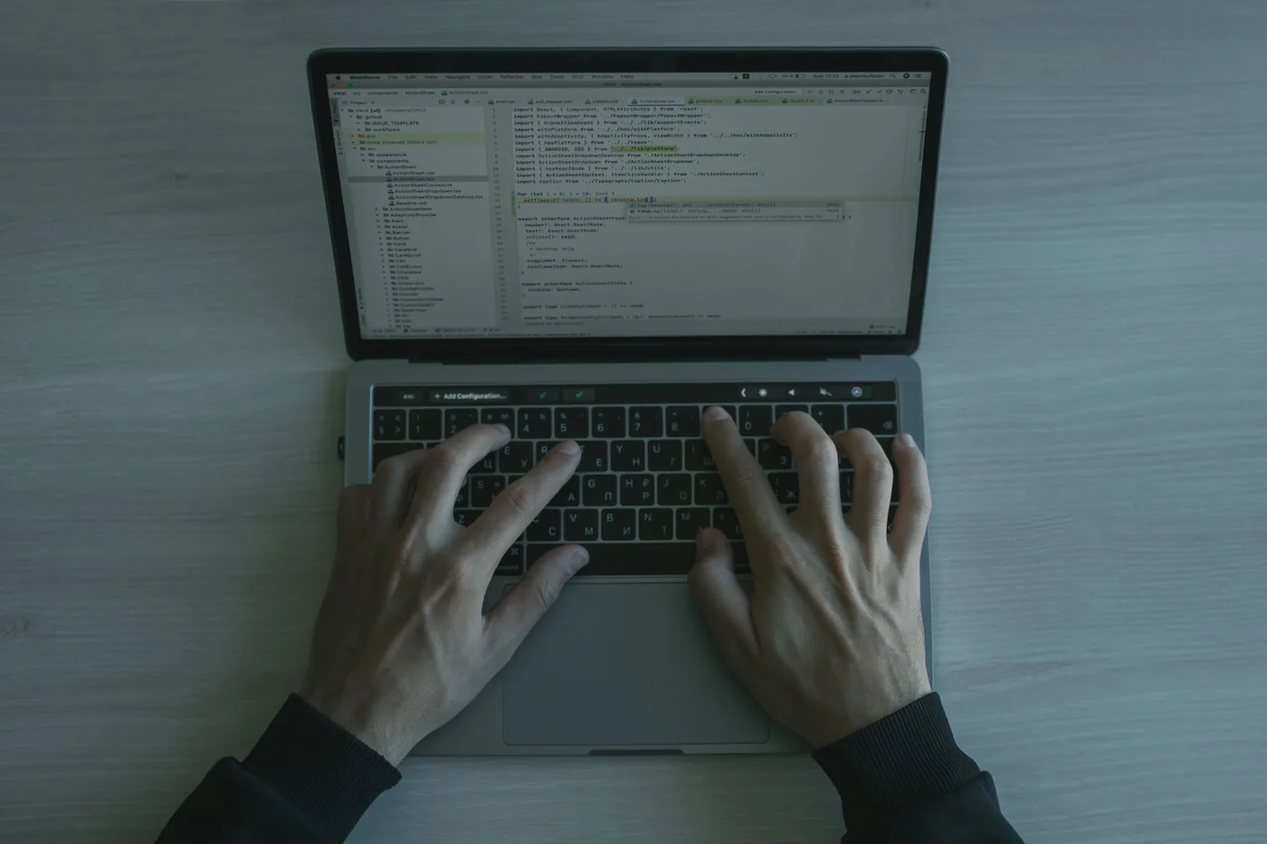 Hands typing on the keyboard of an open laptop with code on the screen