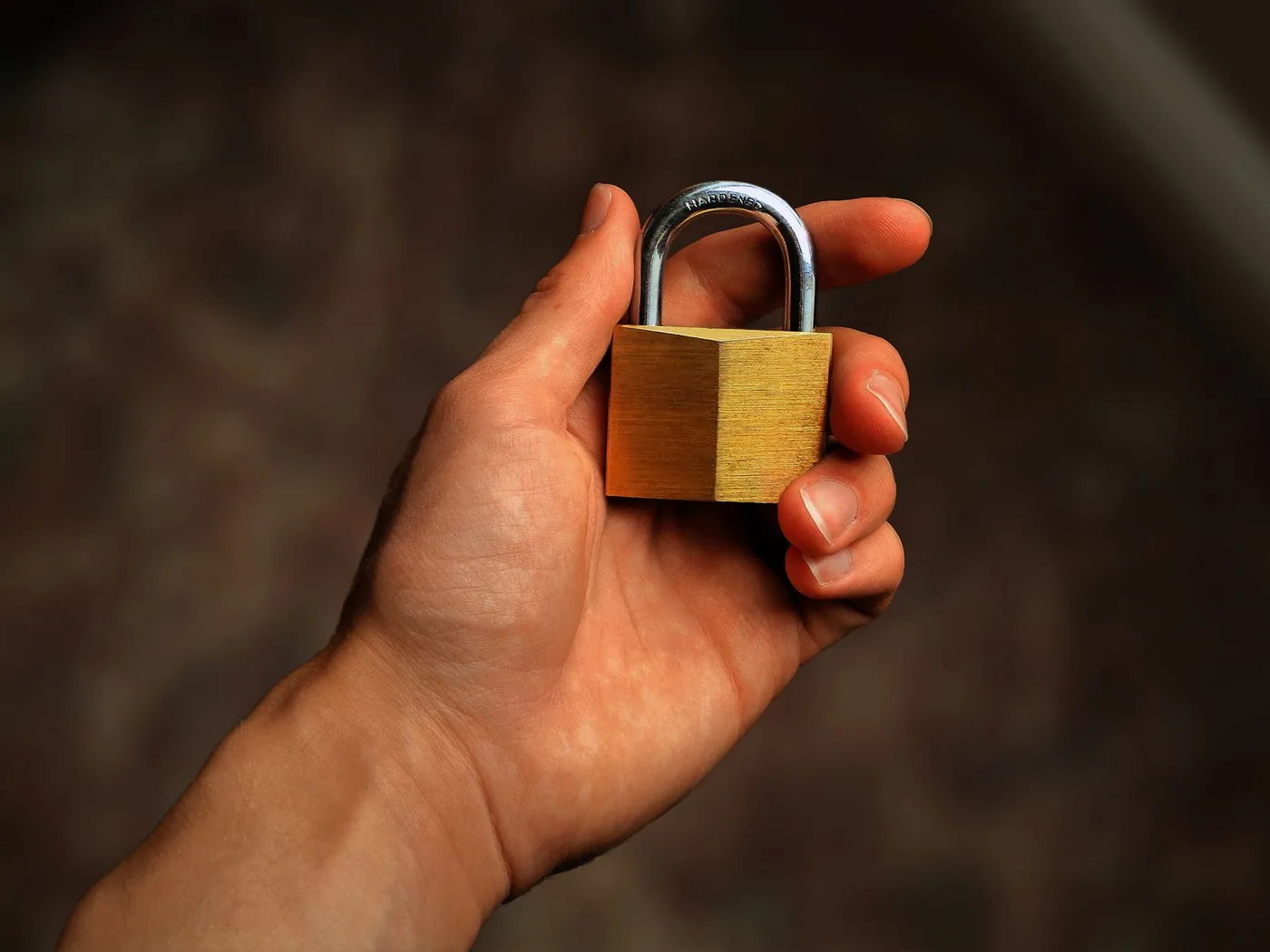 Hand holding a brass padlock against a dark background